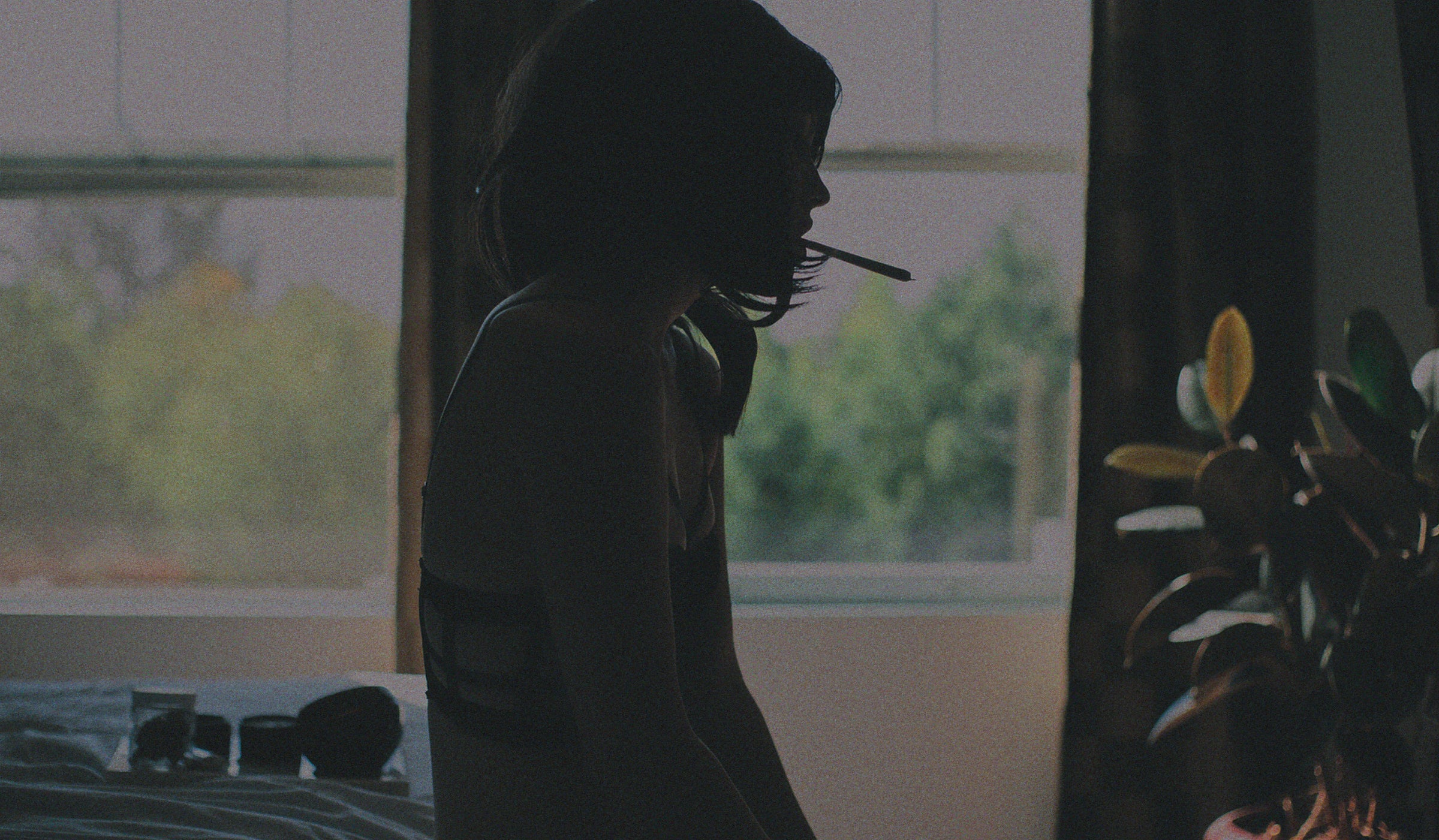 Ethereal glow: A stunning woman in a bedroom, captured in a contre-jour photo, with a cannabis pre-roll gracefully held in her mouth.